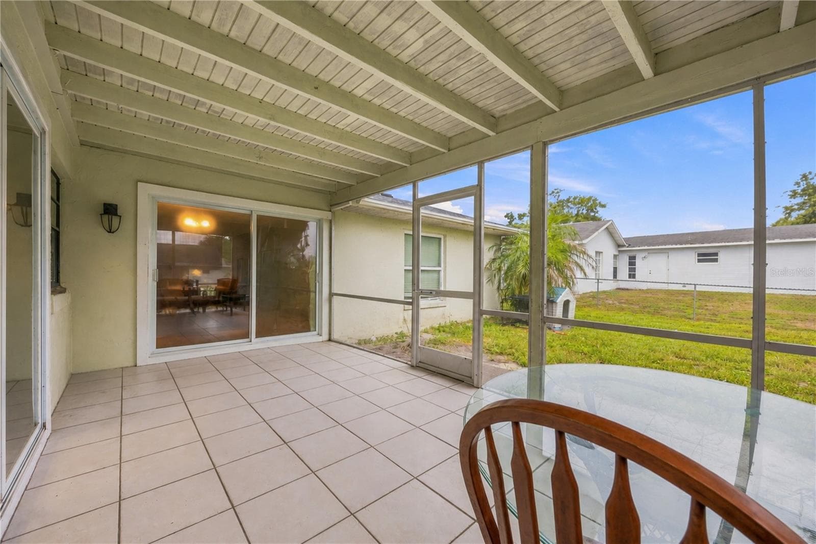 Extended screened back porch featuring tiled flooring, sliding glass door access, and views of the fenced green yard. - 3906 SANTIAGO ST, SEBRING