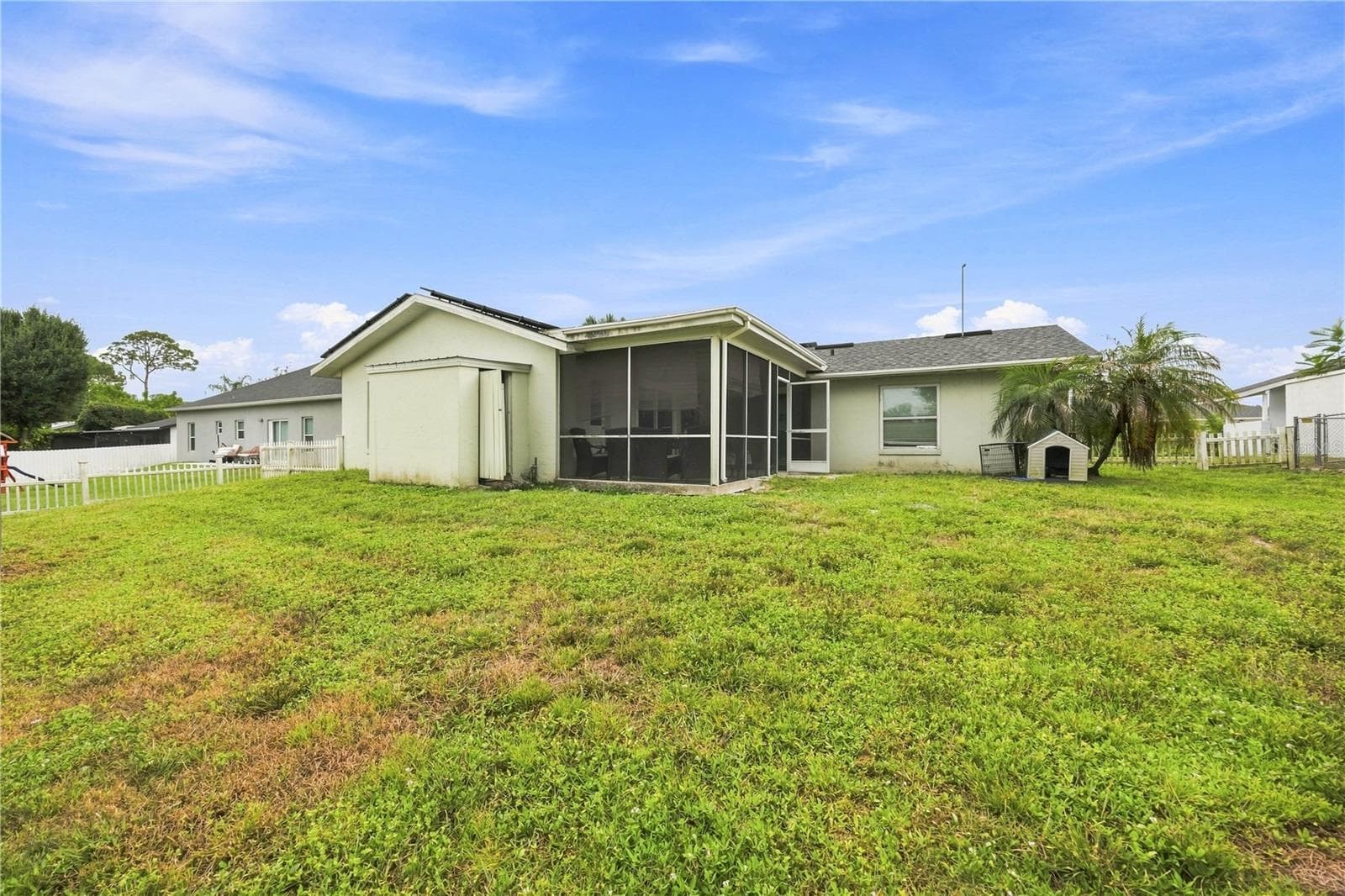 Extended rear view highlighting the large fenced green yard, screened-in lanai access, mature palm, and adjacent detached structure. - 3906 SANTIAGO ST, SEBRING