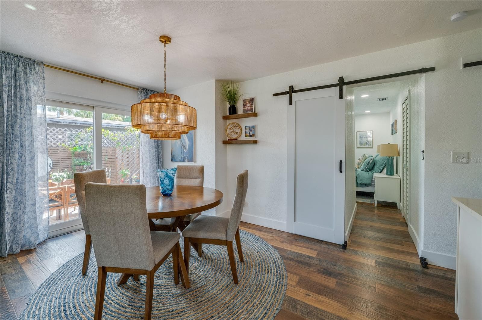 Dedicated dining nook highlighted by a woven pendant light fixture, sliding glass doors to the outside, and a modern white barn door leading down the hallway. - 348 WOODLAND AVE, DAYTONA BEACH