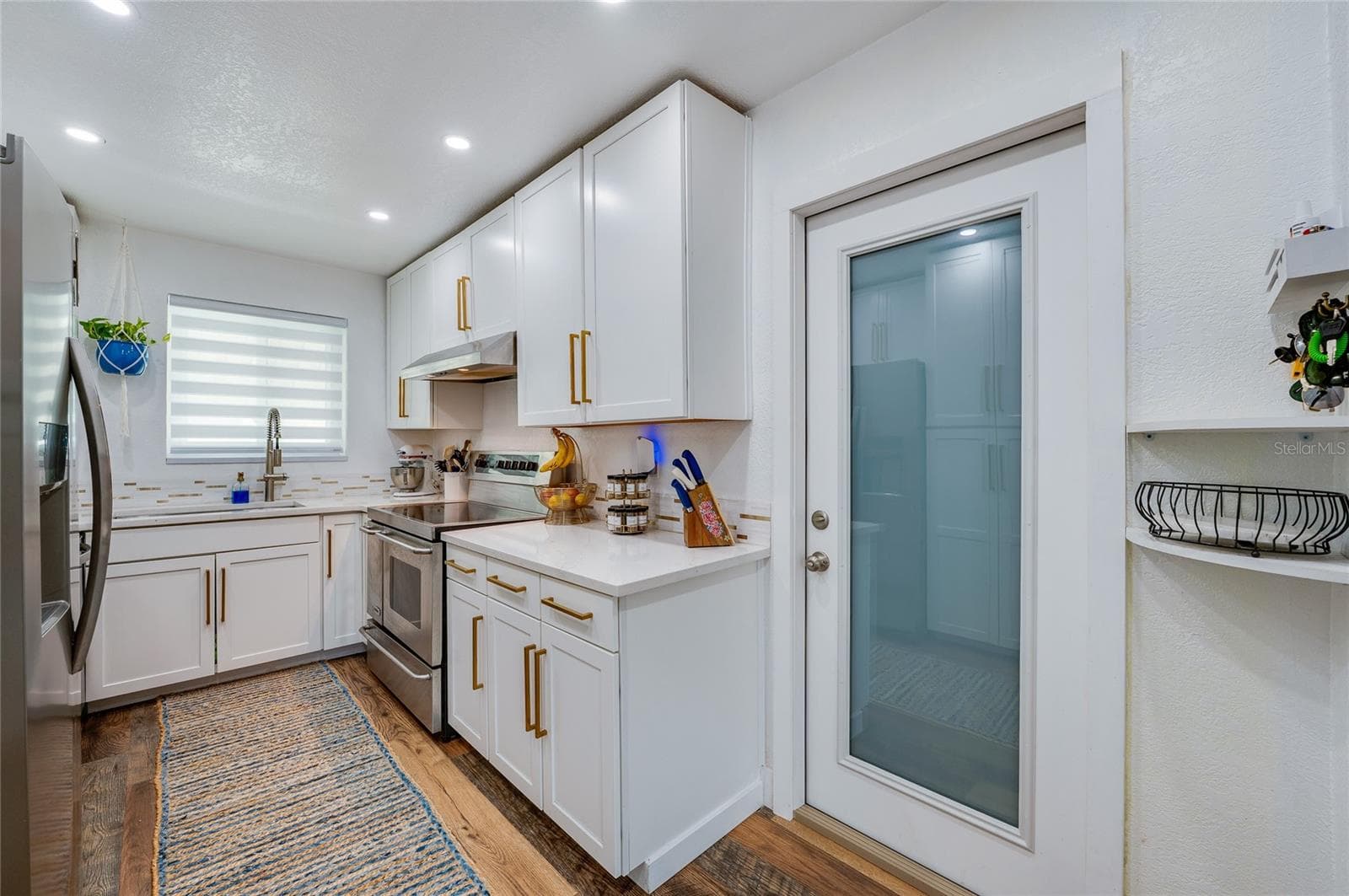 Sleek kitchen space complete with white cabinetry, warm LVP flooring, stainless steel appliances, and a glass-paneled door. - 348 WOODLAND AVE, DAYTONA BEACH