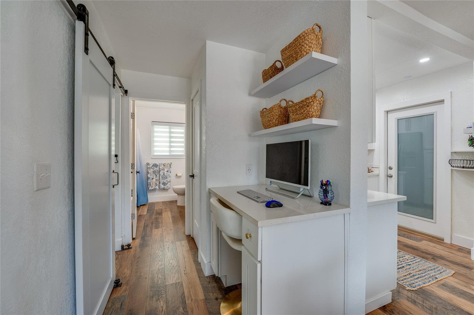 Built-in study alcove with white cabinetry, quartz counter space, and floating shelves, situated in a hallway featuring LVP floors and a sliding barn door. - 348 WOODLAND AVE, DAYTONA BEACH