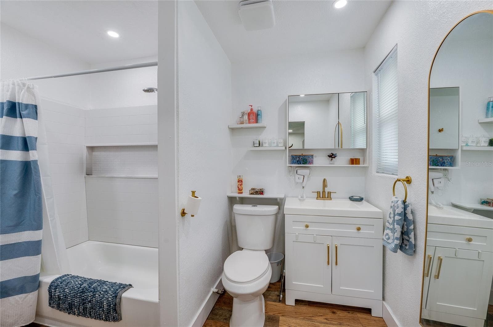 Clean full bathroom featuring a white vanity with gold hardware accents, LVP flooring, and a tub shower combination. - 348 WOODLAND AVE, DAYTONA BEACH