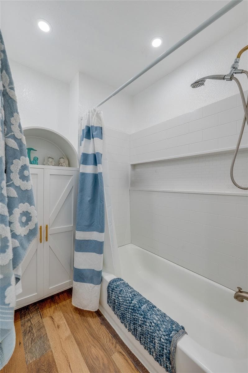 Updated bathroom display showing a white shower surround with built-in storage niches, brushed gold shower fixtures, and a white arched storage cabinet. - 348 WOODLAND AVE, DAYTONA BEACH