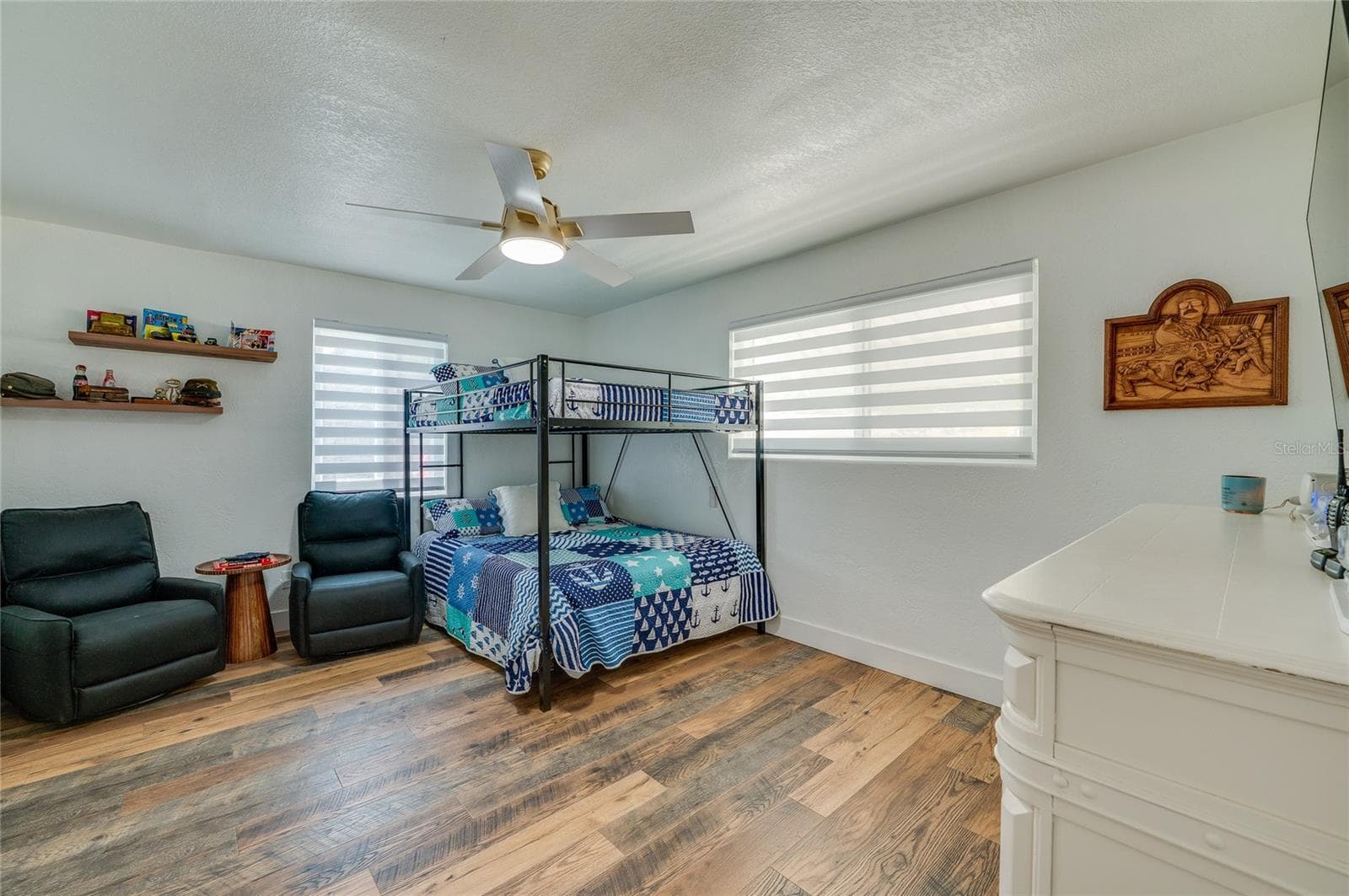 Generous bedroom design highlighting warm LVP flooring, neutral walls, two large windows with blinds, and floating display shelves. - 348 WOODLAND AVE, DAYTONA BEACH