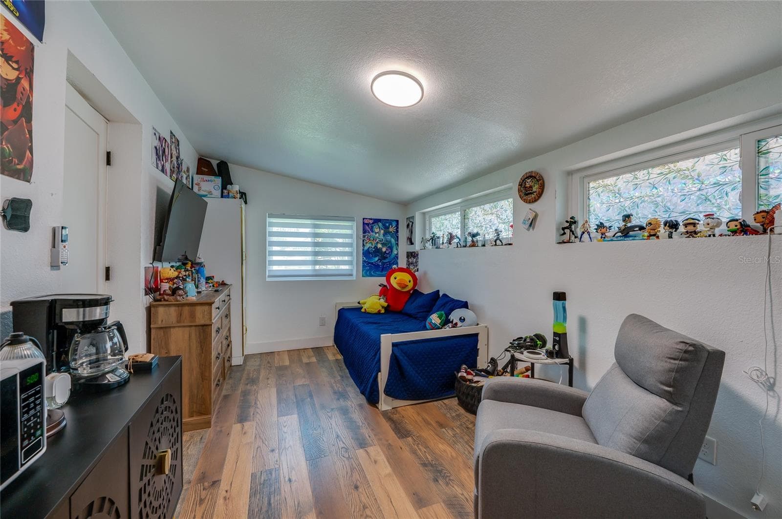 Cozy bedroom featuring LVP flooring, sloped ceilings, ample natural light from multiple windows, and smooth neutral walls. - 348 WOODLAND AVE, DAYTONA BEACH