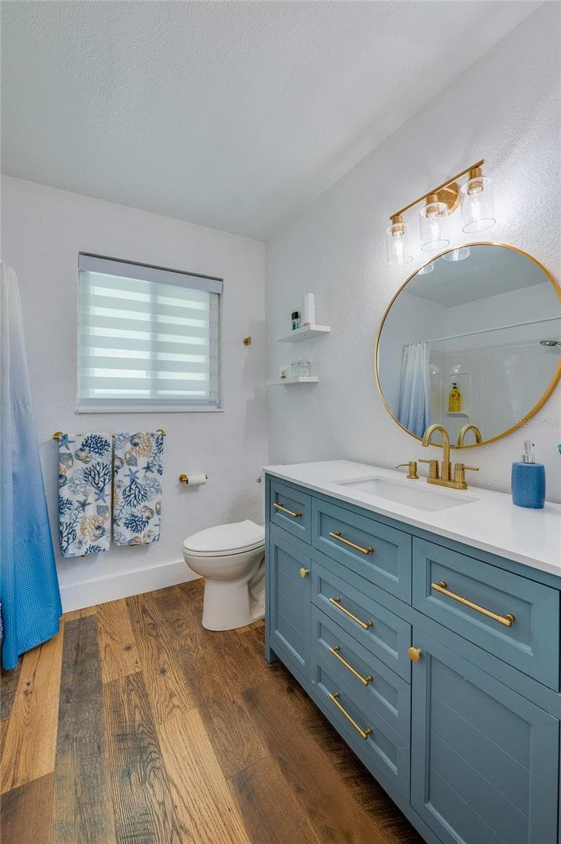 Stylish bathroom featuring a blue vanity with gold hardware, a round brass-framed mirror, and modern lighting. - 348 WOODLAND AVE, DAYTONA BEACH