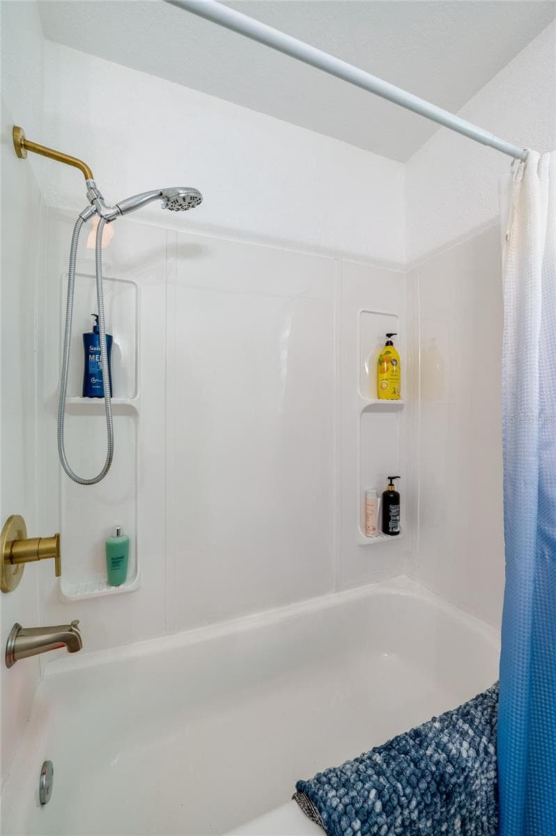 Close-up of a updated bathtub and shower combination complete with a white surround, dual wall niches for toiletries, and warm gold hardware. - 348 WOODLAND AVE, DAYTONA BEACH