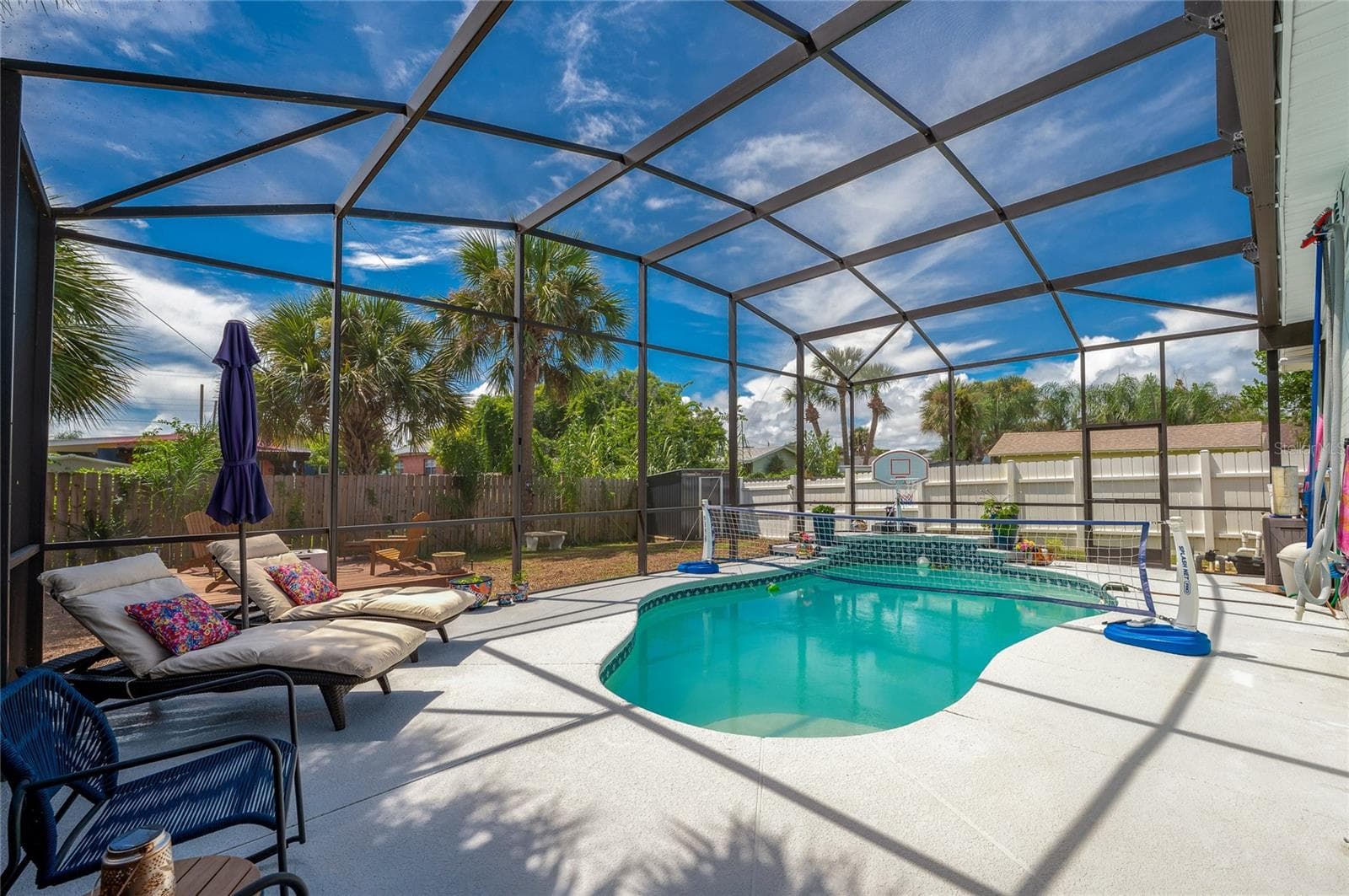 Fully screened pool enclosure featuring a crystal-clear swimming pool. Lush palm trees and a wooden fence surround the perimeter for privacy. - 348 WOODLAND AVE, DAYTONA BEACH