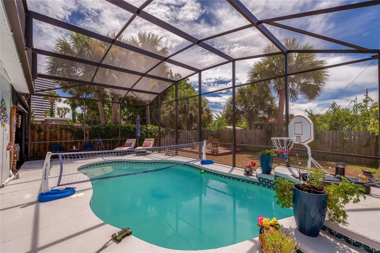 In-ground swimming pool inside a fully screened enclosure. Tiled accents and potted plants border the sunlit pool deck. - 348 WOODLAND AVE, DAYTONA BEACH