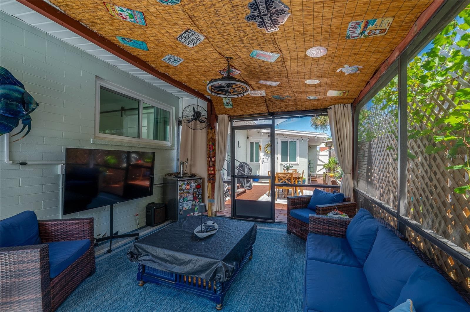 Inviting screened-in patio area with decorative bamboo ceiling panels and sheer privacy curtains. It offers clear views leading out to the sunlit outdoor deck. - 348 WOODLAND AVE, DAYTONA BEACH