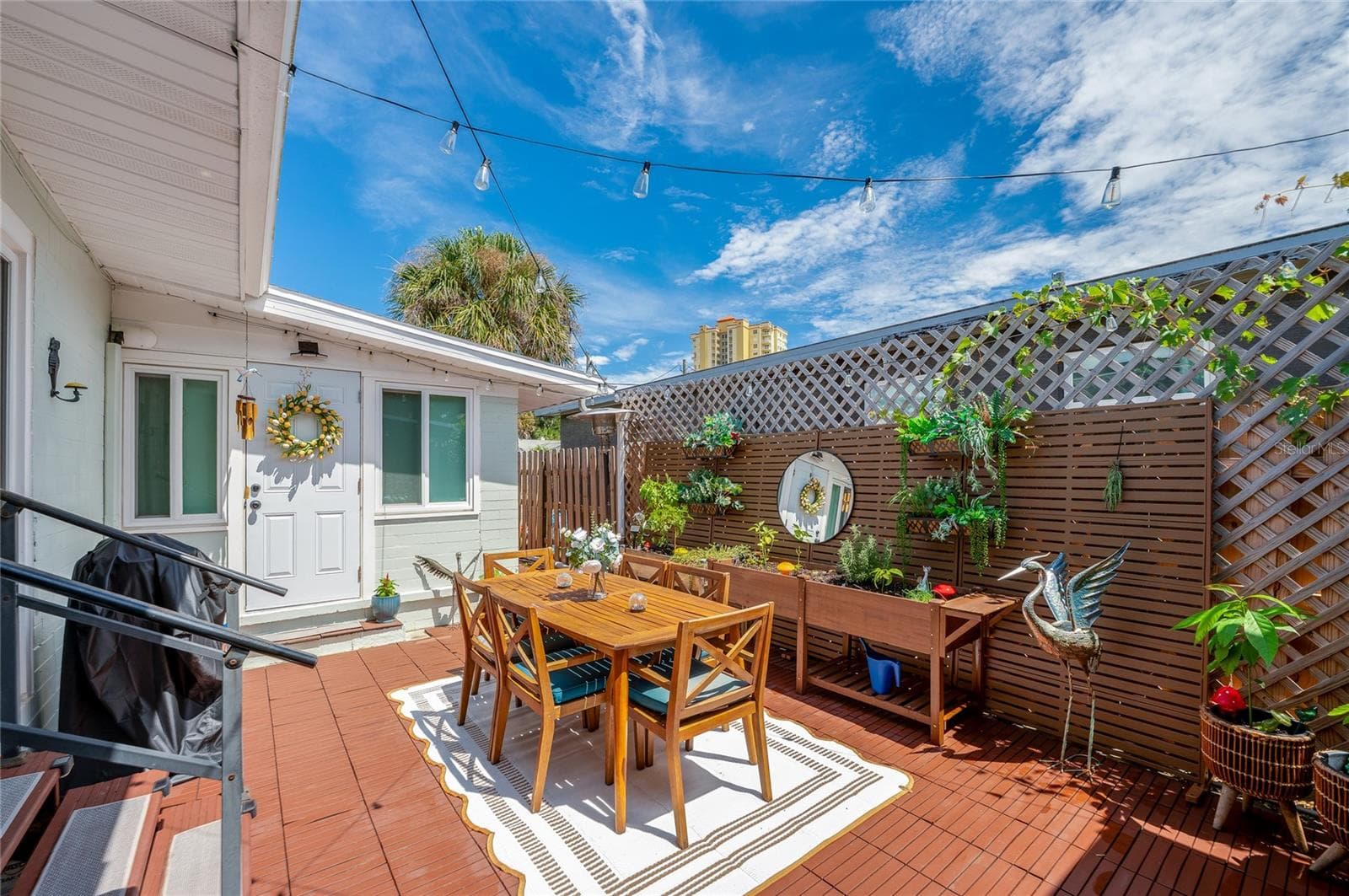 Charming outdoor wooden deck framed by lattice fencing, ambient string lights, and potted greenery. An entryway with a decorative wreath adds a welcoming touch. - 348 WOODLAND AVE, DAYTONA BEACH