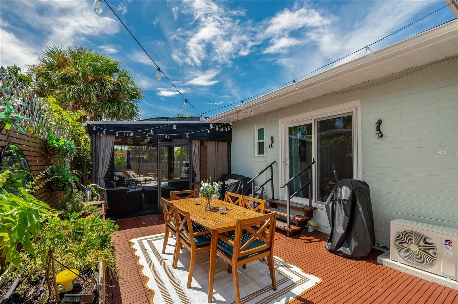 Spacious outdoor patio area with dark wooden decking, sliding glass door access, and string lights overhead. The space includes raised garden planters and a adjacent screen enclosure. - 348 WOODLAND AVE, DAYTONA BEACH