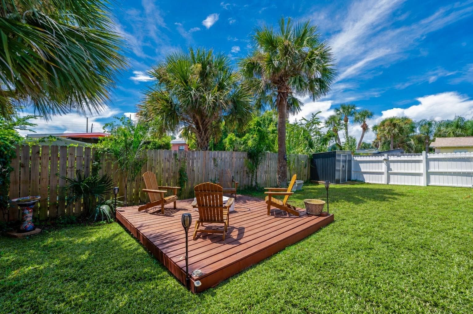 Raised wooden deck platform set within a private, fully fenced backyard. Tall palm trees overhead provide natural shade and tropical ambiance. - 348 WOODLAND AVE, DAYTONA BEACH