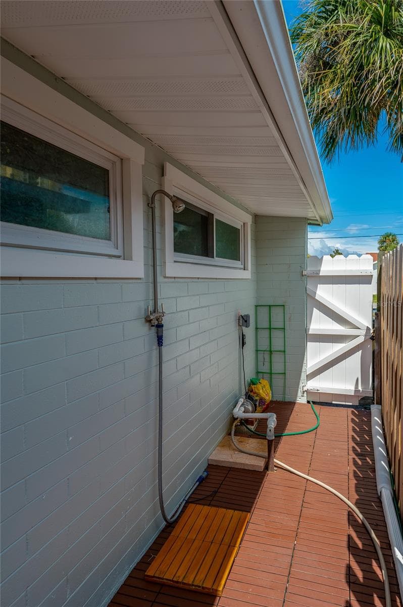 Convenient outdoor shower station installed along the side exterior wall with a wooden foot mat. A white vinyl gate provides privacy and secure access to the yard. - 348 WOODLAND AVE, DAYTONA BEACH
