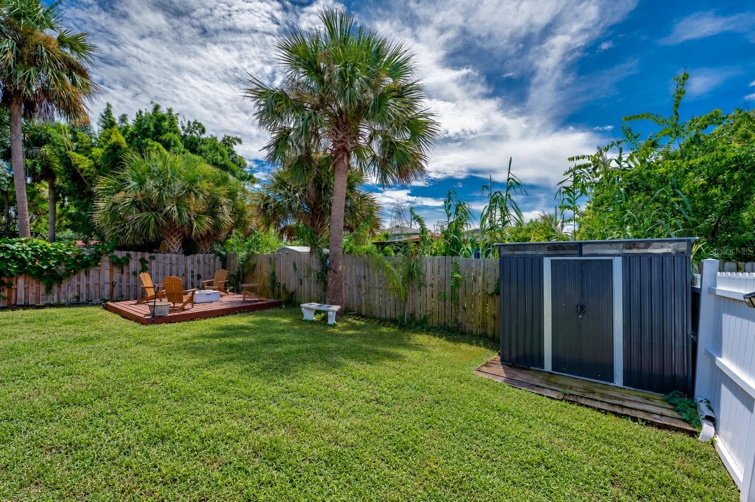 Fenced backyard area featuring a standalone storage shed and mature palm trees. A raised wooden platform sits tucked in the corner of the yard. - 348 WOODLAND AVE, DAYTONA BEACH