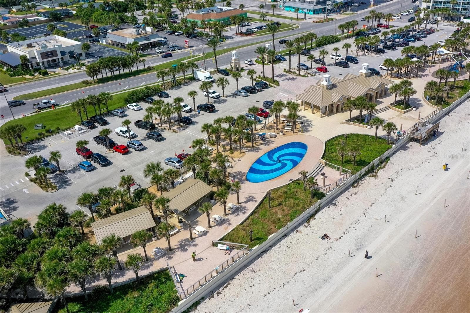 Sweeping aerial view captures Andy Romano Beachfront Park along the Atlantic coastline, featuring beachfront recreation areas, landscaped grounds, parking, and direct access to the sand. - 348 WOODLAND AVE, DAYTONA BEACH
