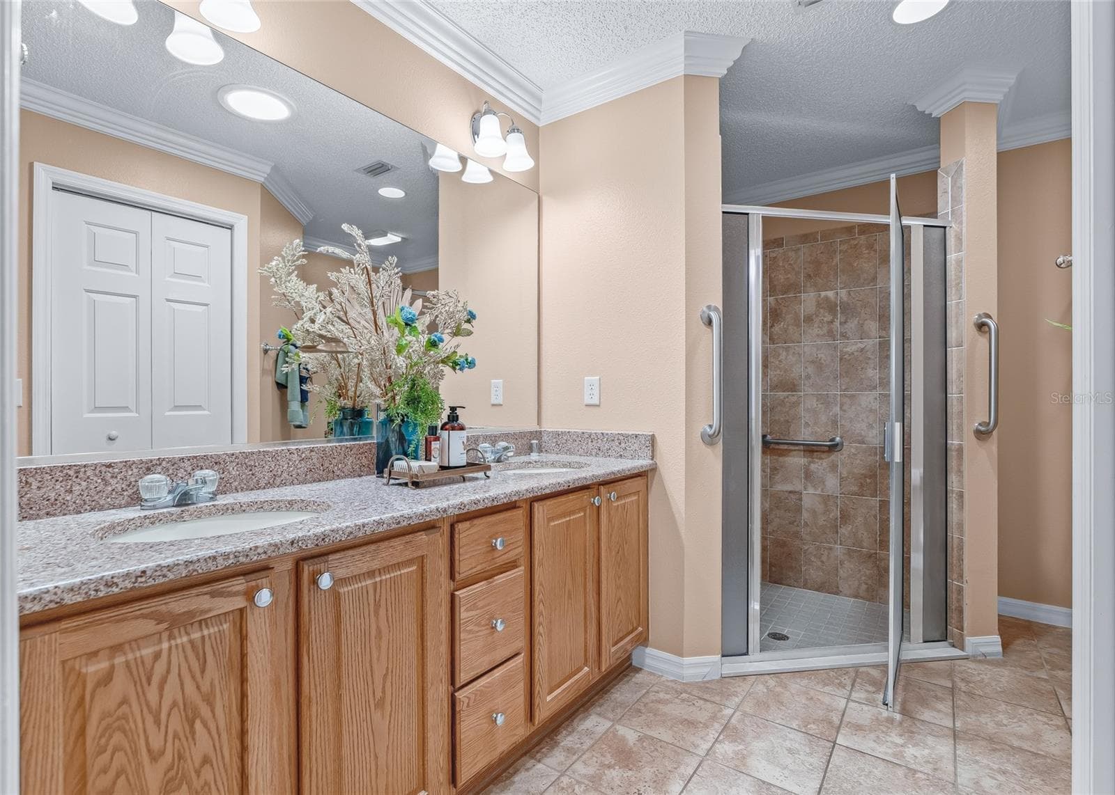 Spacious Primary Bath features a long dual-sink vanity, extensive cabinetry, large mirror, recessed lighting and a beautifully tiled walk-in shower. - 17601 SE 81ST TIMBERWOOD TER, THE VILLAGES