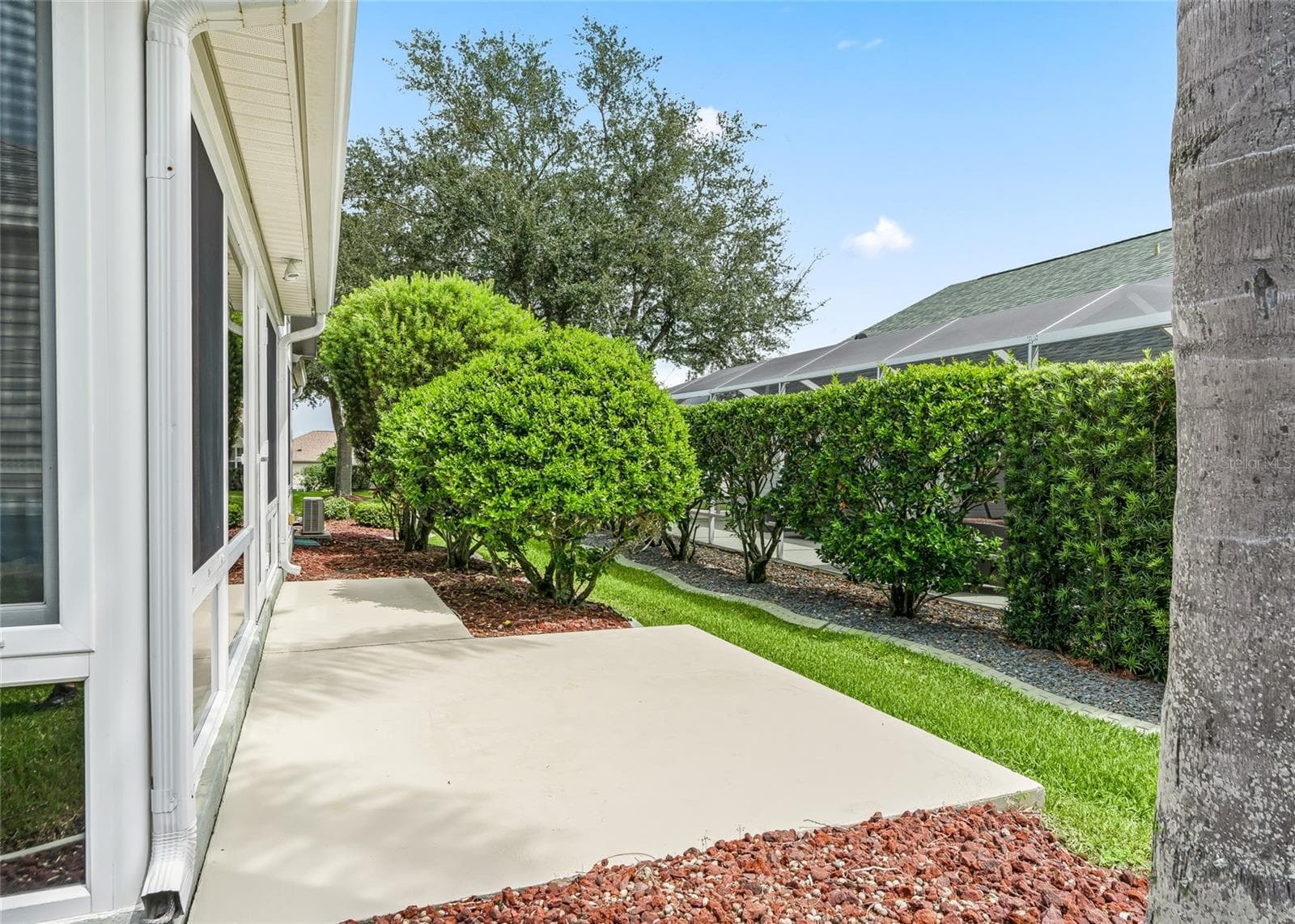 Concrete patio area beside the Florida Room offers additional outdoor space for grilling, seating or enjoying the Florida sunshine, bordered by mature landscaping. - 17601 SE 81ST TIMBERWOOD TER, THE VILLAGES