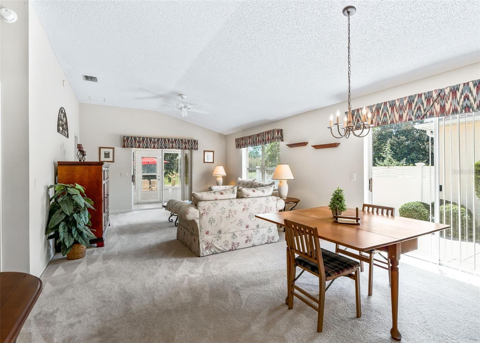 Spacious living area featuring vaulted ceilings and a bright, open feel. Two sets of doors provide convenient access to both the outdoor patio and enclosed lanai, creating a seamless connection between the indoor and outdoor living spaces. - 17535 SE 84TH FOXGROVE AVE, THE VILLAGES