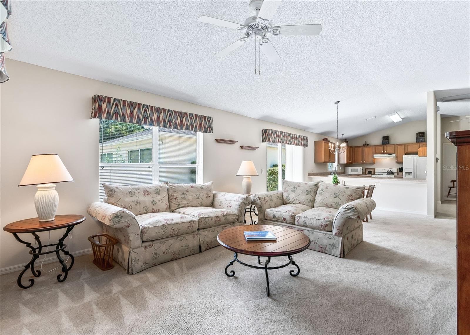 Bright, comfortable, and open living space featuring high ceilings that create an airy, spacious feel. A ceiling fan adds comfort, while sliding doors provide easy access to the outdoors. The living area flows seamlessly into the dining and kitchen spaces, creating a wonderful open layout perfect for relaxing and entertaining. - 17535 SE 84TH FOXGROVE AVE, THE VILLAGES