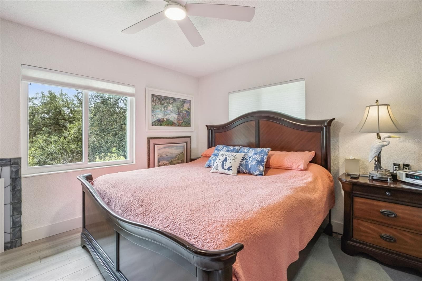 Retreat to the relaxing primary suite featuring a cozy fireplace accent, ceiling fan, and serene tree-top views through oversized windows. - 1476 SPRING LAKE RD, FRUITLAND PARK