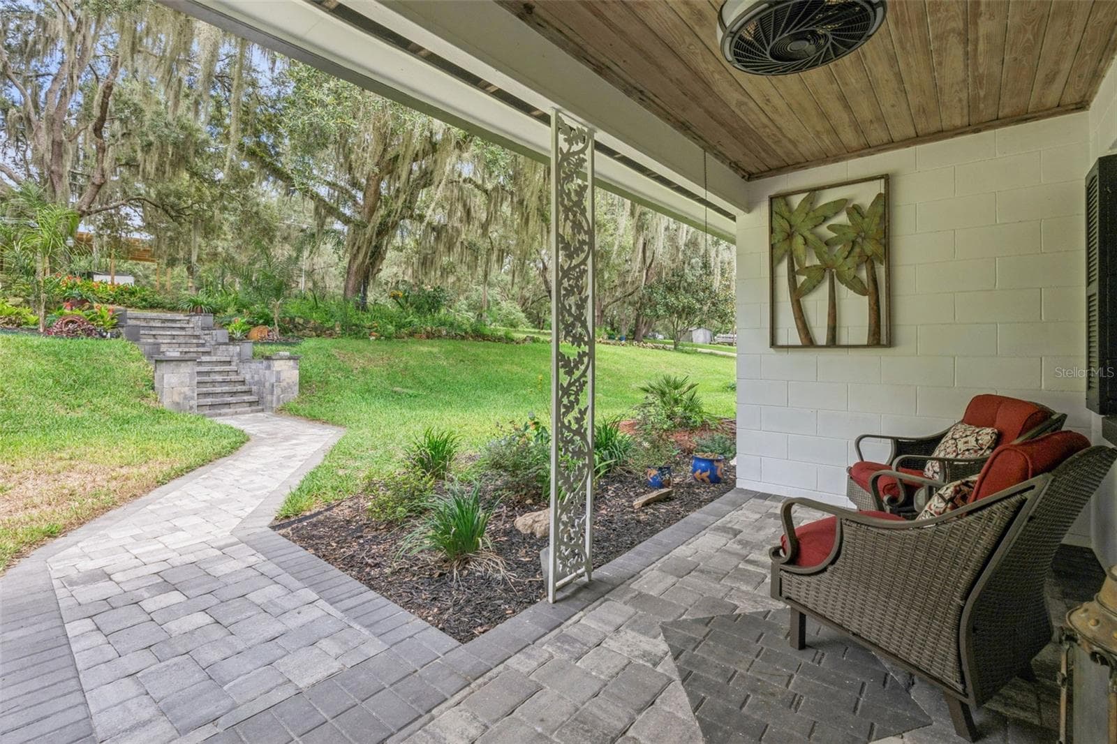 Covered lower patio with paver stone flooring, a decorative trellis, and a paver walkway leading through the lush, shaded yard. - 1476 SPRING LAKE RD, FRUITLAND PARK