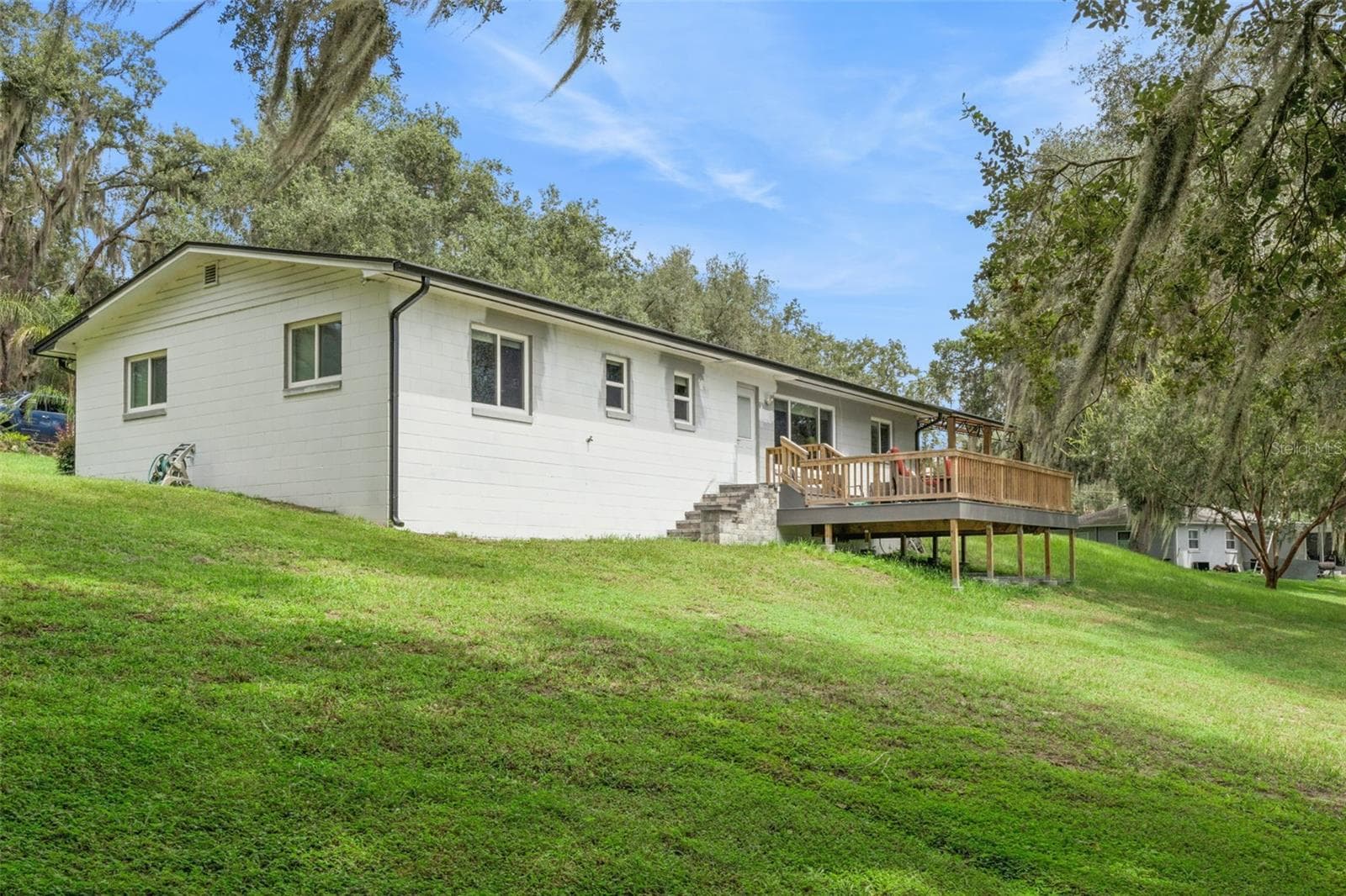 Rear view of the home showcasing the elevated deck, manicured lawn, and the natural beauty of Central Florida's rolling landscape. - 1476 SPRING LAKE RD, FRUITLAND PARK