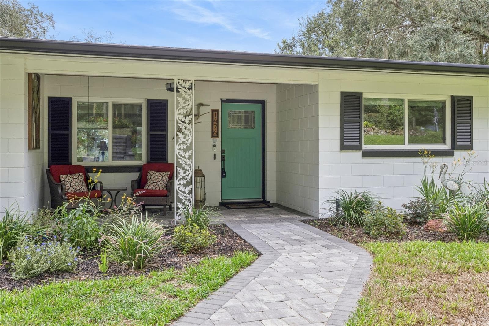 Step onto the welcoming front porch featuring paver stone, comfortable seating, and lush garden views. - 1476 SPRING LAKE RD, FRUITLAND PARK