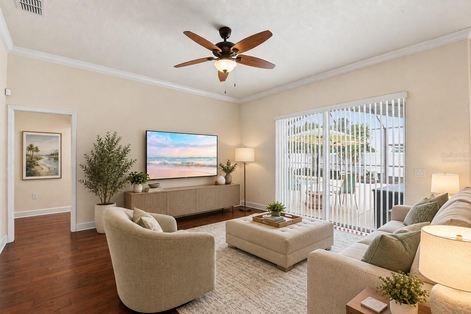 Living Room – Virtually staged to illustrate furnishing possibilities, this bright living room features warm wood flooring, crown molding, a ceiling fan, and wide sliding glass doors opening to the outdoor living and pool area. - 114 VIOLA DR, AUBURNDALE