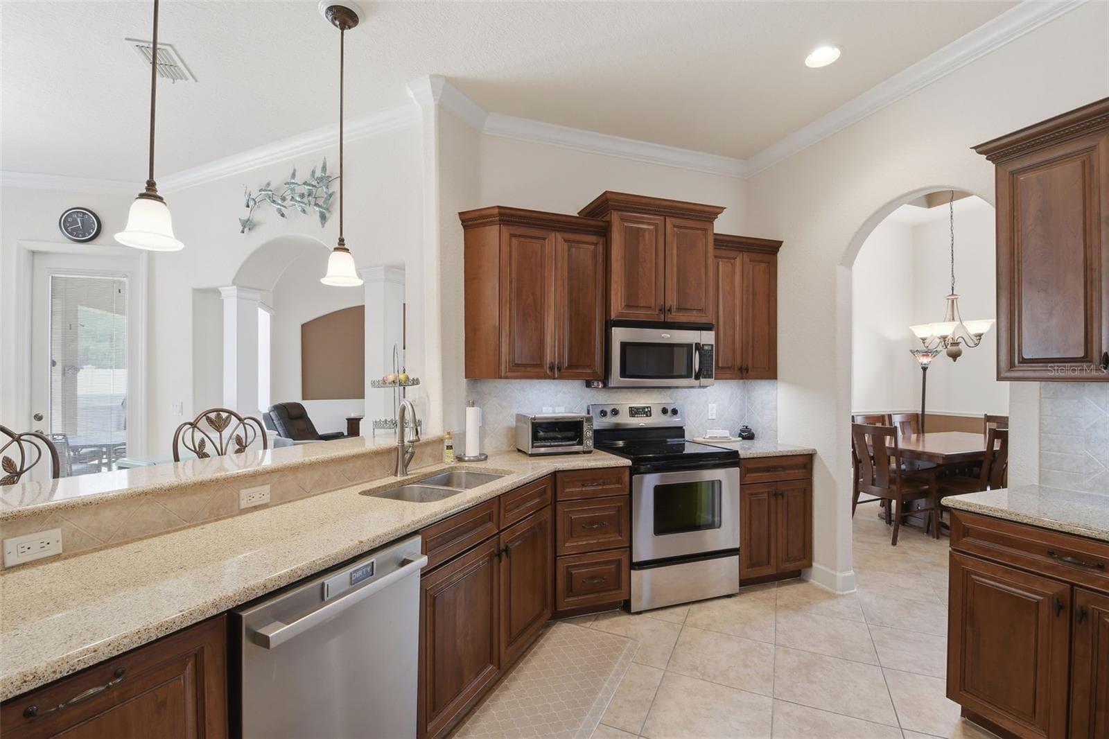 Kitchen – Well-appointed kitchen featuring warm wood cabinetry, granite countertops, stainless steel appliances, tile backsplash, and a breakfast bar that opens toward the adjacent living space. - 114 VIOLA DR, AUBURNDALE