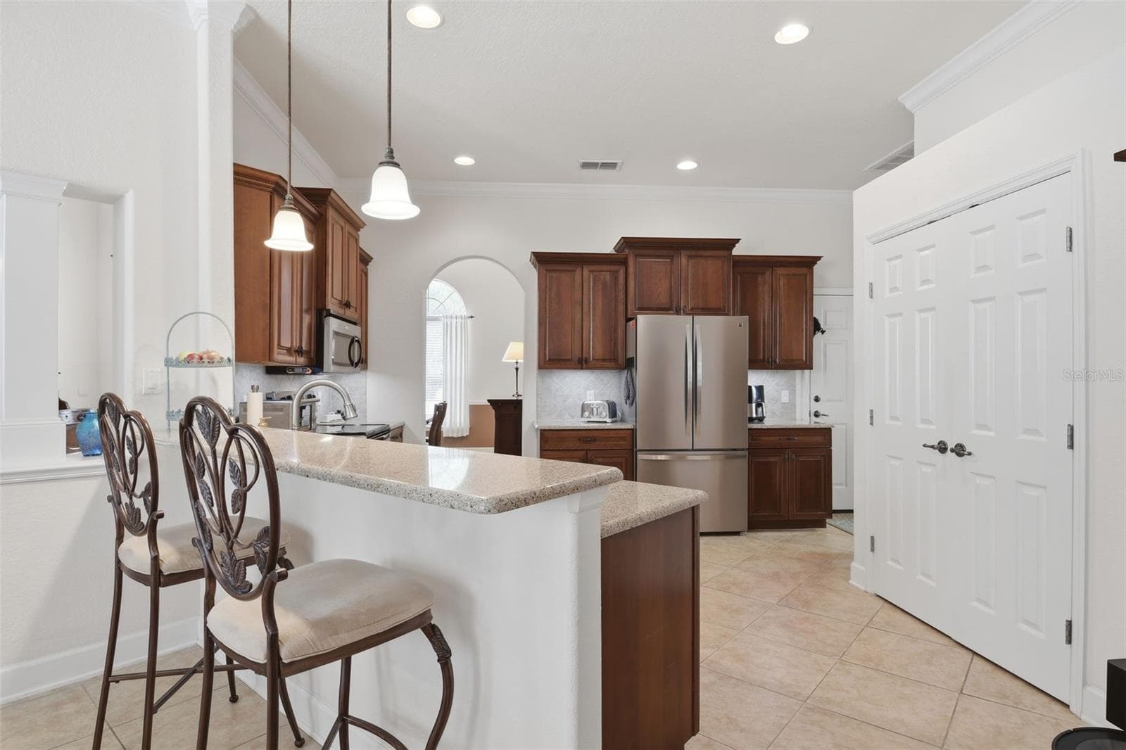 Kitchen / Breakfast Bar – The kitchen offers an extended breakfast bar with pendant lighting, warm wood cabinetry, stainless steel appliances, and ample counter space for casual dining and meal prep. - 114 VIOLA DR, AUBURNDALE