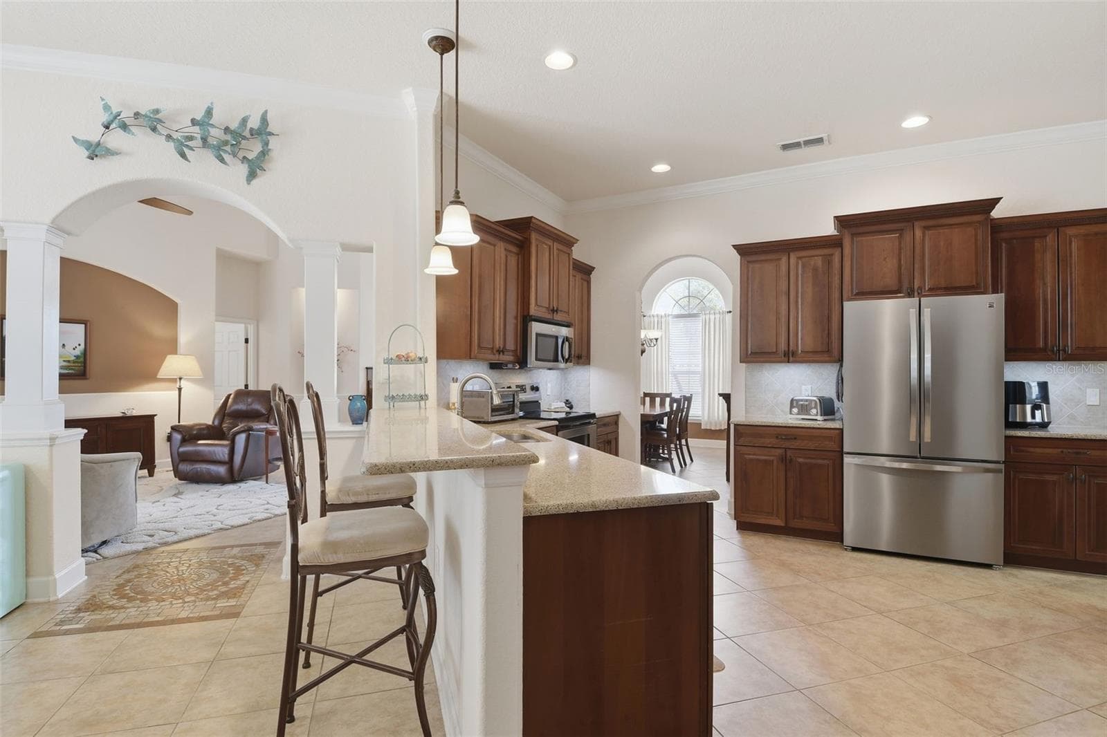 Kitchen / Open Layout – A wider kitchen view highlights the open connection to the adjoining living area, along with abundant cabinetry, recessed lighting, and a spacious peninsula with bar seating. - 114 VIOLA DR, AUBURNDALE