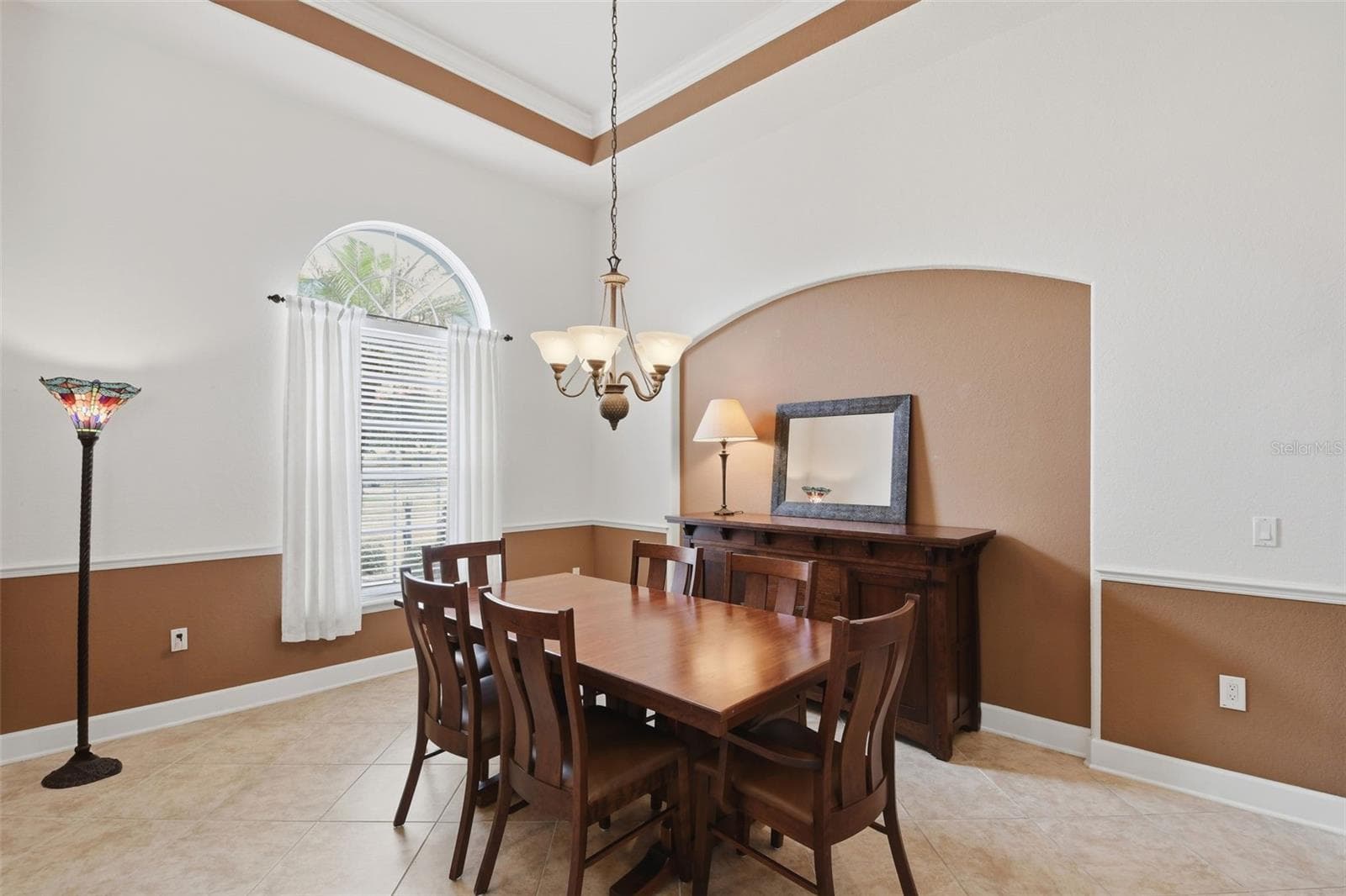 Dining Room – Formal dining space with a tray ceiling, chandelier, arched window, and decorative wall detailing that adds architectural interest. - 114 VIOLA DR, AUBURNDALE