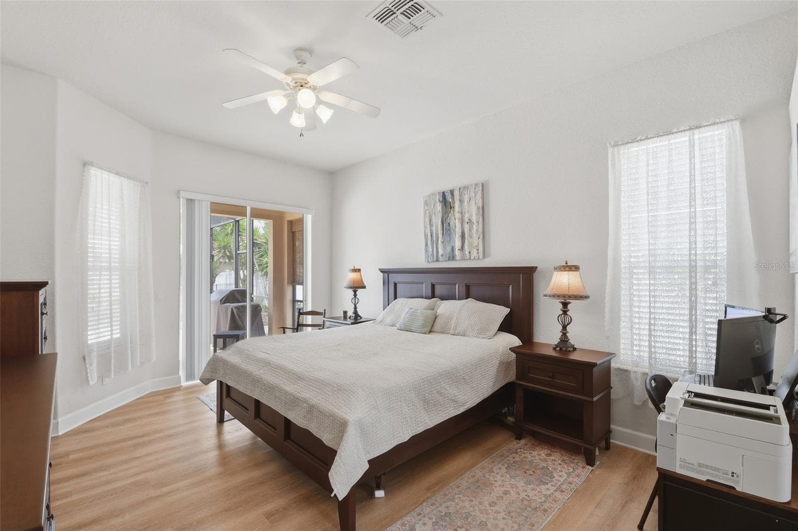 Primary Bedroom – Spacious primary bedroom with wood-look flooring, a ceiling fan, abundant natural light, and sliding glass doors providing direct access to the covered outdoor area - 114 VIOLA DR, AUBURNDALE