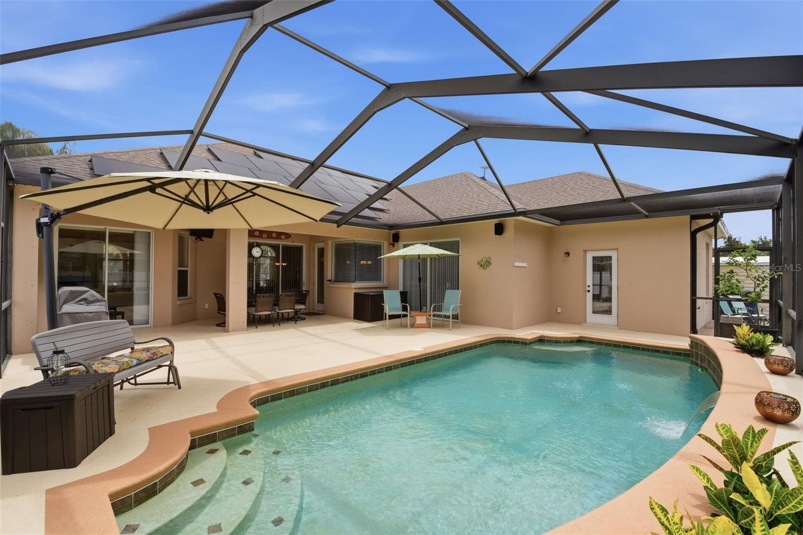 Pool – Another angle showcases the pool’s entry steps, curved design, and water feature, with the covered outdoor living area just beyond. - 114 VIOLA DR, AUBURNDALE