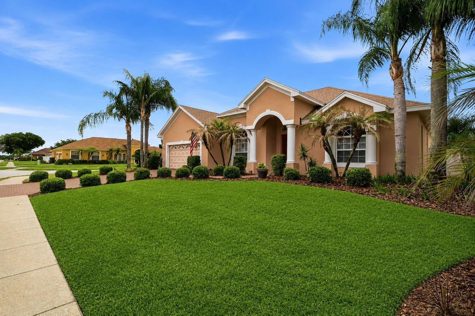 Front Exterior – Welcoming single-story exterior framed by mature palms and manicured landscaping, with an arched entry, column accents, and a spacious green lawn. - 114 VIOLA DR, AUBURNDALE