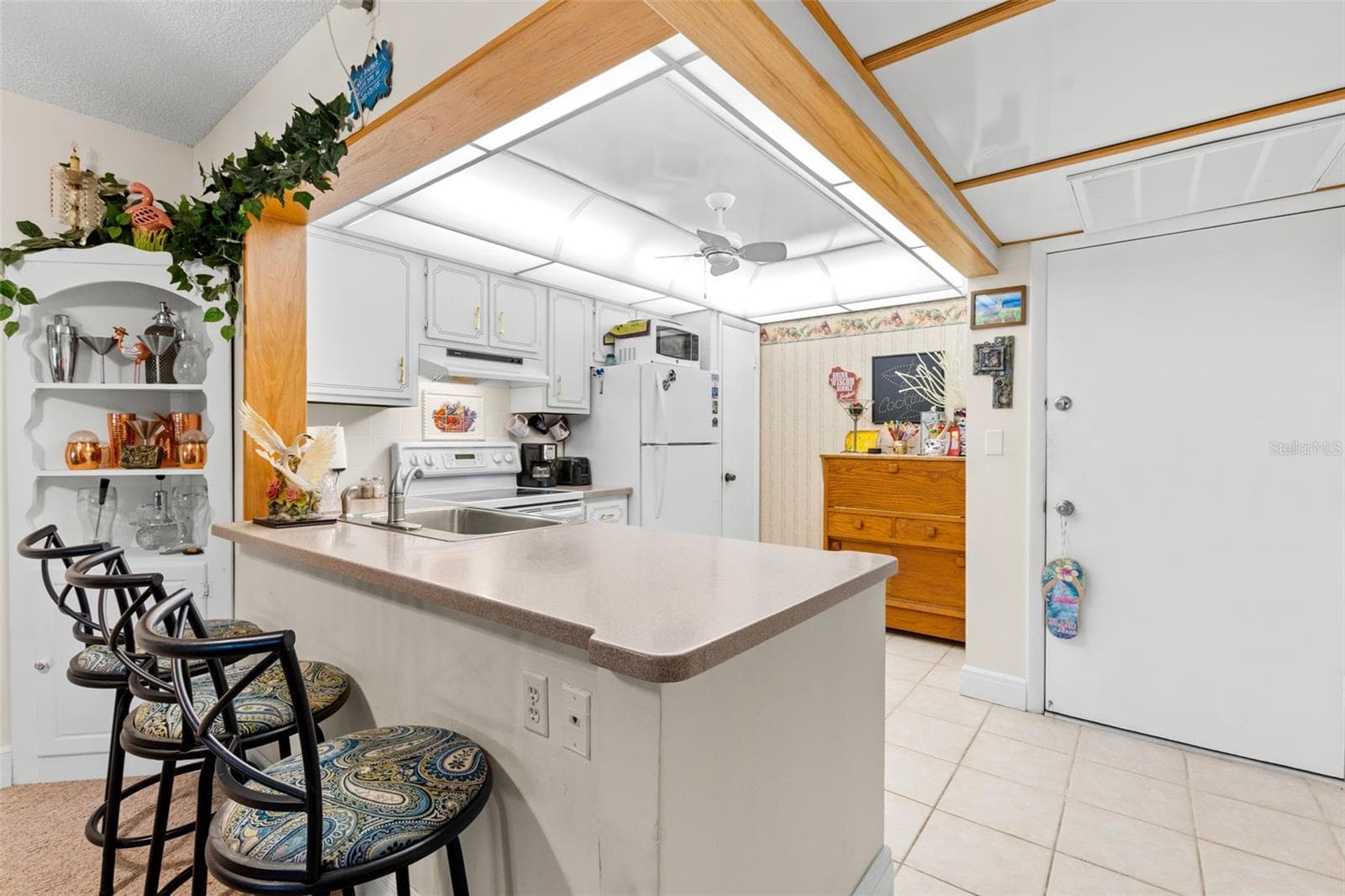 Just inside the entry, the kitchen wraps around a wide peninsula with bar seating, generous counter space and open shelving nearby. The raised ceiling detail continues overhead, while the open layout keeps the kitchen connected to the dining and living areas beyond. - 12300 VONN RD #3204, LARGO