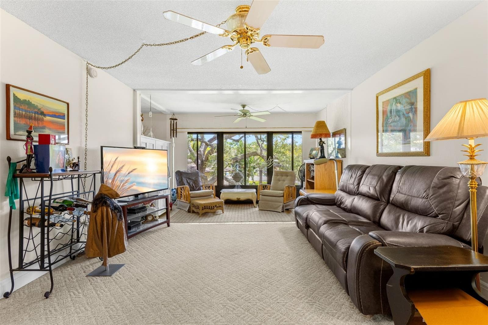 The living room stretches toward a wall of windows overlooking mature trees, with neutral carpeting and ceiling fans throughout. The length of the room also allows for a separate sitting area at the far end without crowding the main seating space. - 12300 VONN RD #3204, LARGO