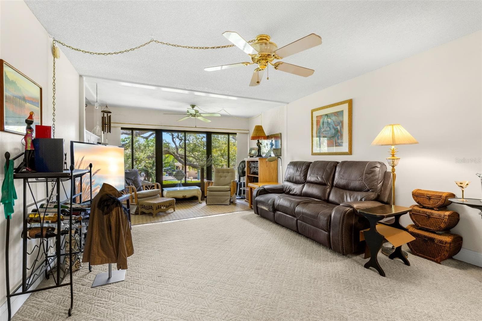 The living room extends into an enclosed Florida room, where a broad wall of windows brings in natural light and frames the mature trees outside. The extra space works comfortably as a second sitting area without interrupting the main living room. - 12300 VONN RD #3204, LARGO