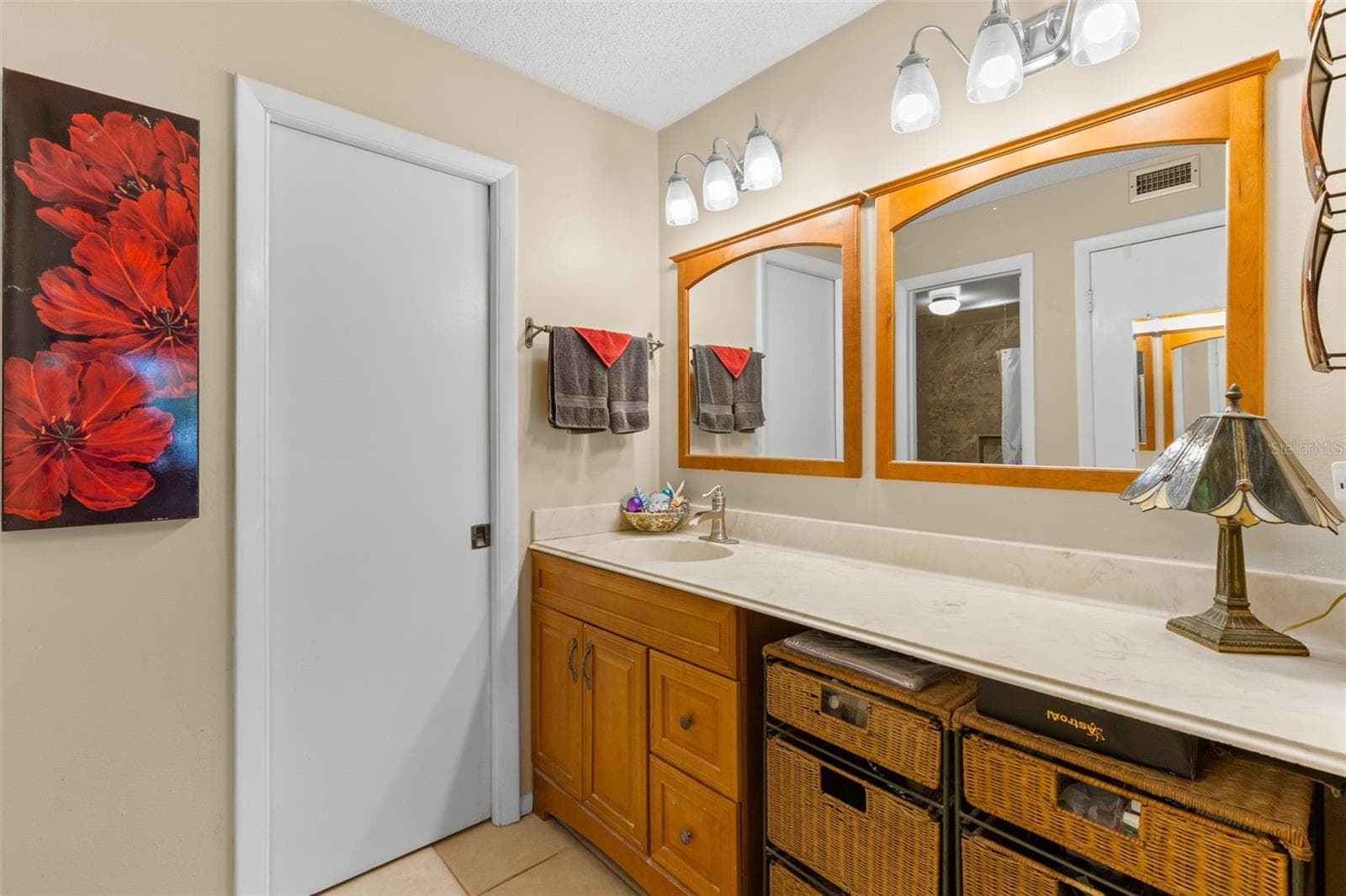 The primary bath pairs warm wood cabinetry with a long counter, framed mirrors and vanity lighting. A single sink leaves generous counter space, while the open knee space beside it provides a dedicated makeup/vanity area. - 12300 VONN RD #3204, LARGO