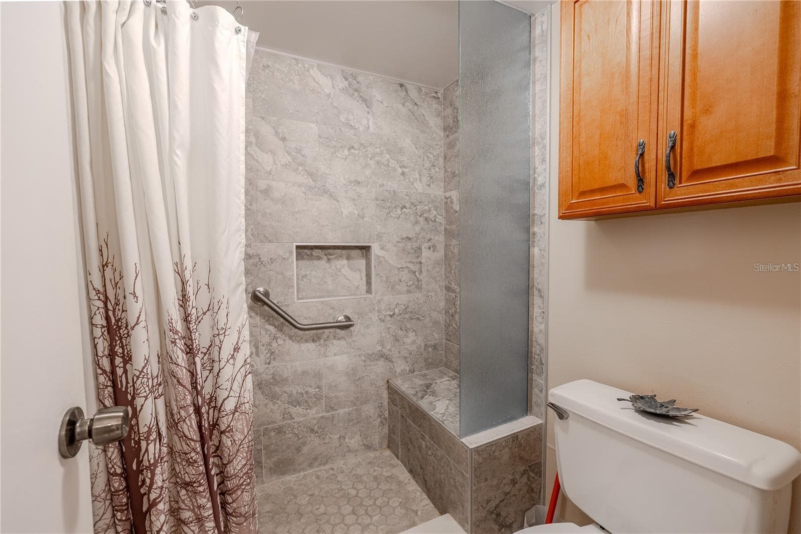 The primary bath includes a tiled walk-in shower with a built-in bench, recessed niche and grab bar. A tall textured-glass panel adds separation, while the wood cabinet above the toilet provides extra storage. - 12300 VONN RD #3204, LARGO