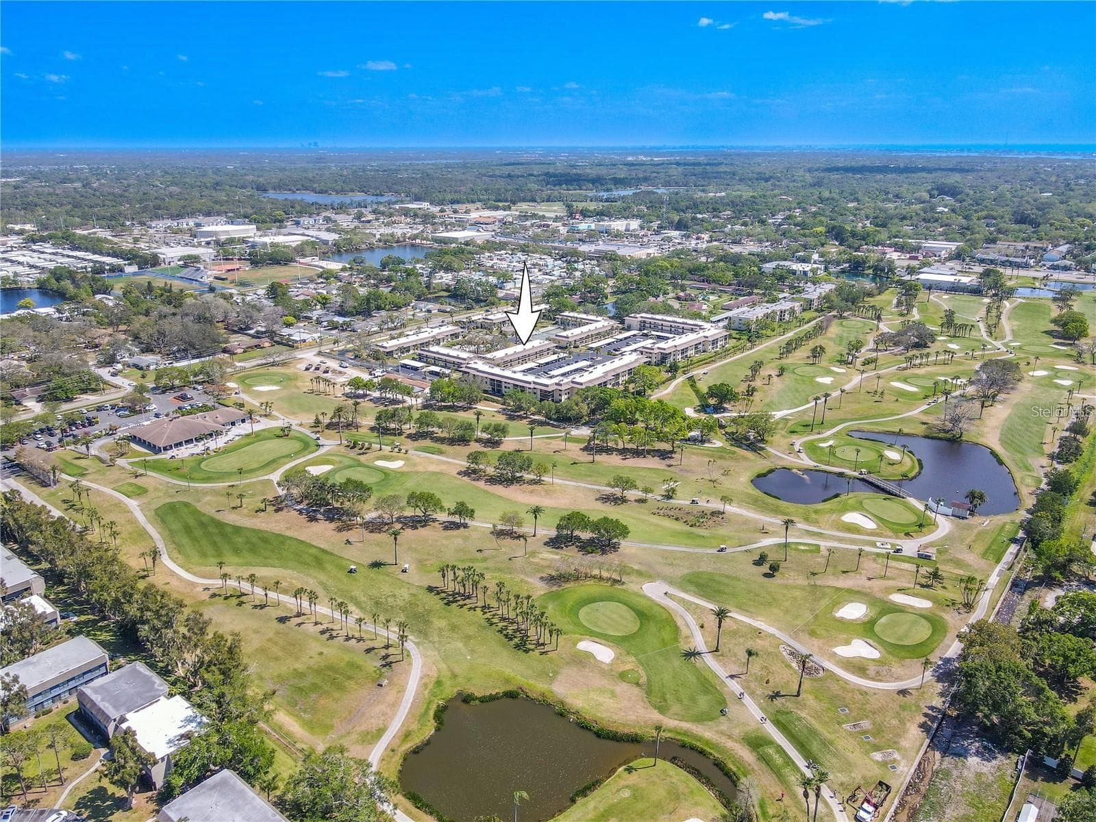Villas de Golf is arranged around landscaped grounds with the community pool and tennis courts near the center, while the neighboring golf course stretches along the east side of the property and the Gulf sits in the distance. - 12300 VONN RD #3204, LARGO