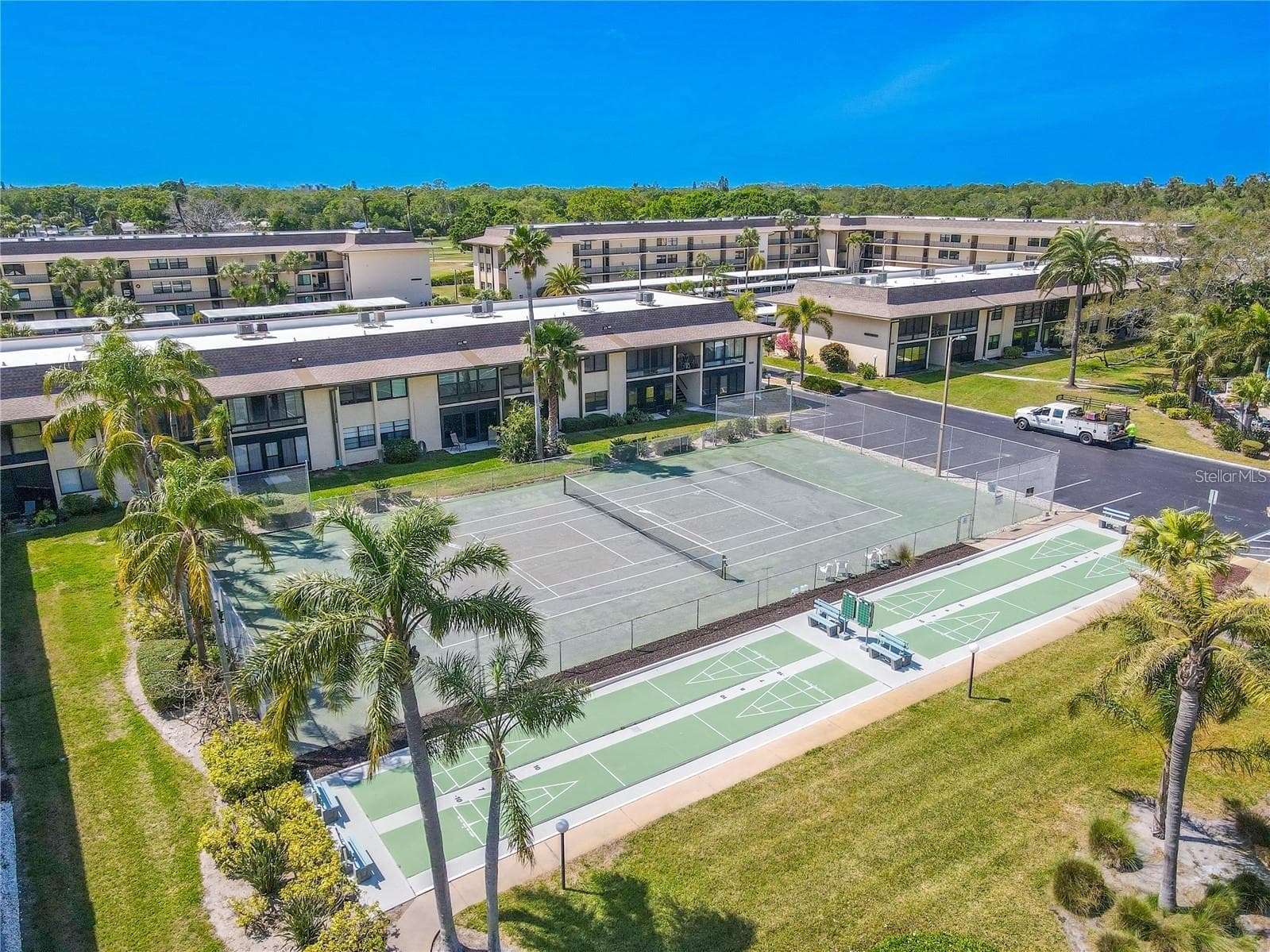 The community recreation area includes a full tennis court and multiple shuffleboard courts, with seating nearby and landscaped grounds surrounding the space. - 12300 VONN RD #3204, LARGO