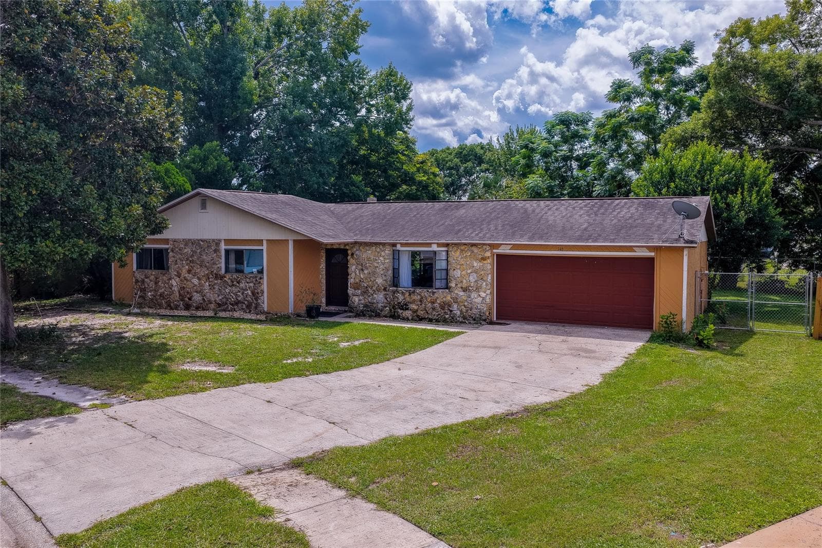 Charming single-story ranch home featuring a stone-accented facade, attached two-car garage, and an expansive paved driveway framed by lush green lawns and mature trees. - 146 WESTWOOD DR, DAYTONA BEACH