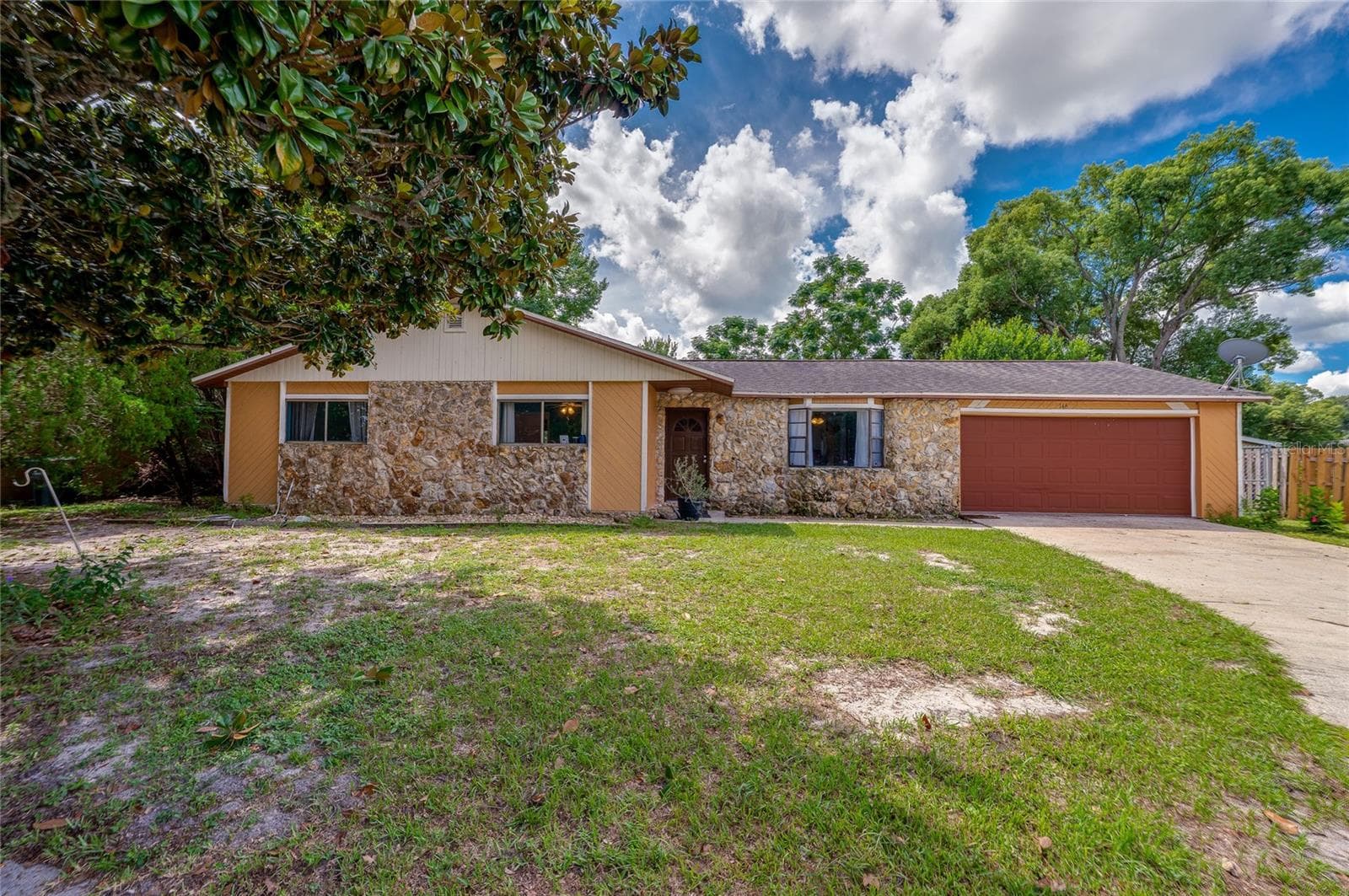 Front exterior of the ranch-style house showcasing decorative stone accent walls, a red garage door, concrete driveway, and front lawn. - 146 WESTWOOD DR, DAYTONA BEACH