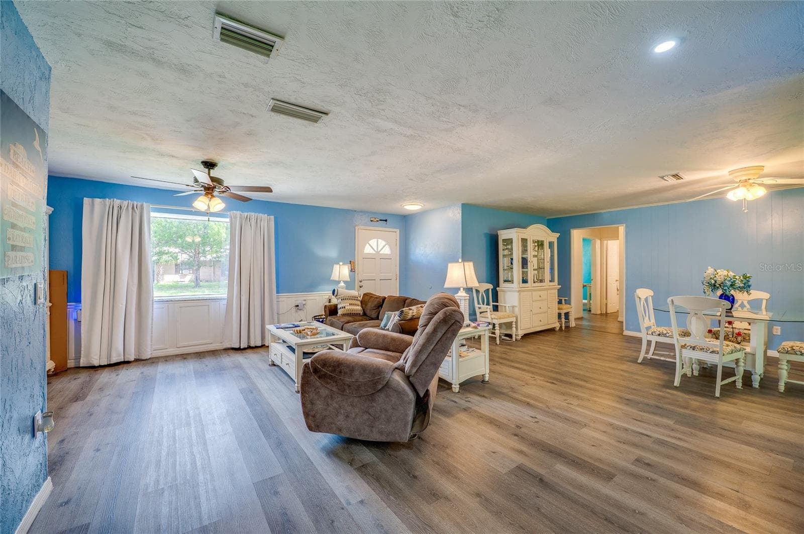 Spacious main living area displaying LVP flooring, light blue walls, a wide window bringing in natural light, and smooth transitions to adjoining rooms. - 146 WESTWOOD DR, DAYTONA BEACH