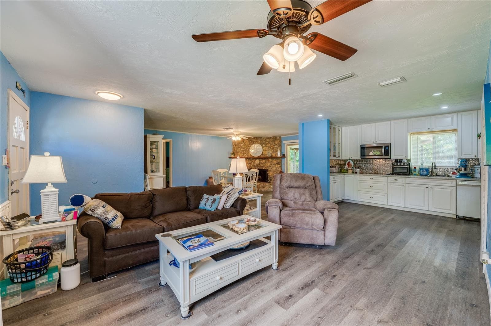 Bright open-concept living area with LVP flooring, cool blue walls, and a ceiling fan leading into the adjacent kitchen and dining spaces. - 146 WESTWOOD DR, DAYTONA BEACH