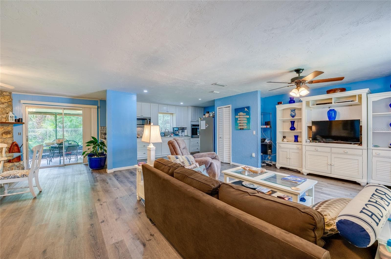 Expansive open living space featuring LVP flooring, bright blue walls, and a large built-in media center. Sliding glass doors open to the adjacent screened patio area. - 146 WESTWOOD DR, DAYTONA BEACH