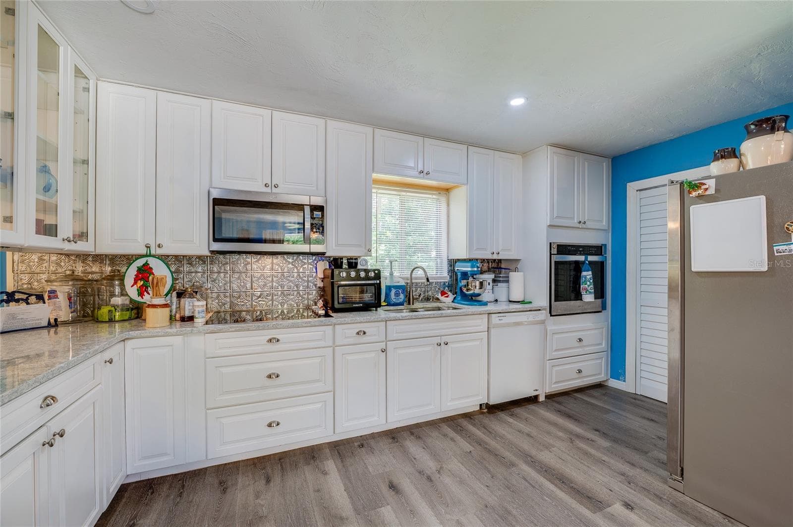 Well-equipped kitchen featuring crisp white cabinetry, textured tile backsplash, built-in appliances, and light grey LVP flooring. - 146 WESTWOOD DR, DAYTONA BEACH