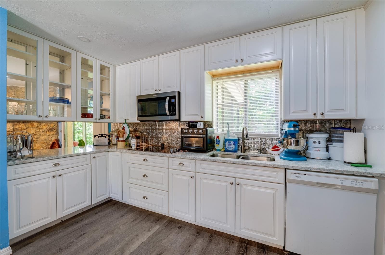Functional kitchen layout complete with white cabinetry, glass-front upper cupboards, a double sink under a bright window, and built-in appliances. - 146 WESTWOOD DR, DAYTONA BEACH